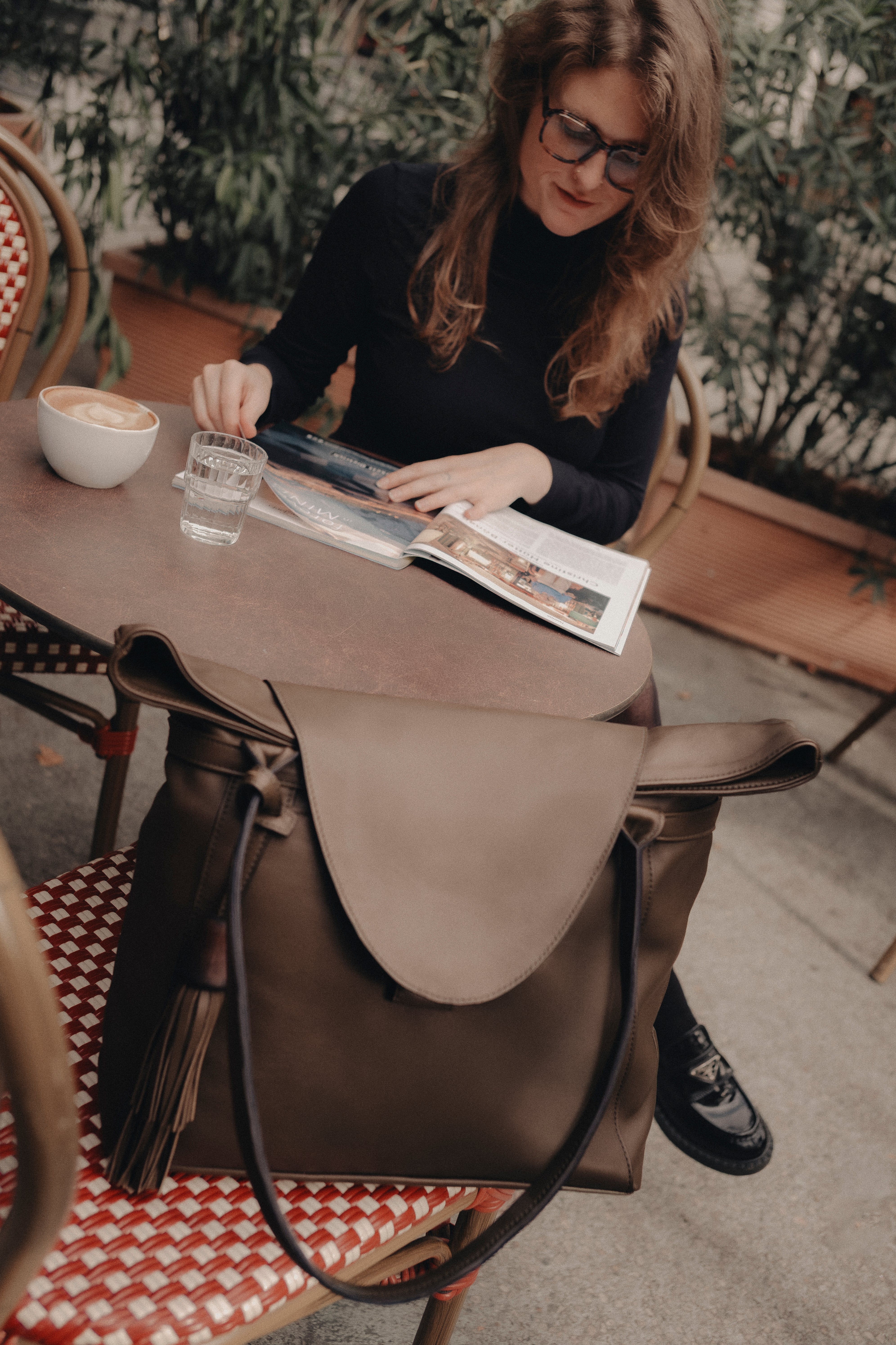 Model sitzt am Tisch, auf dem Stuhl eine braune ABURY Shopper Tasche