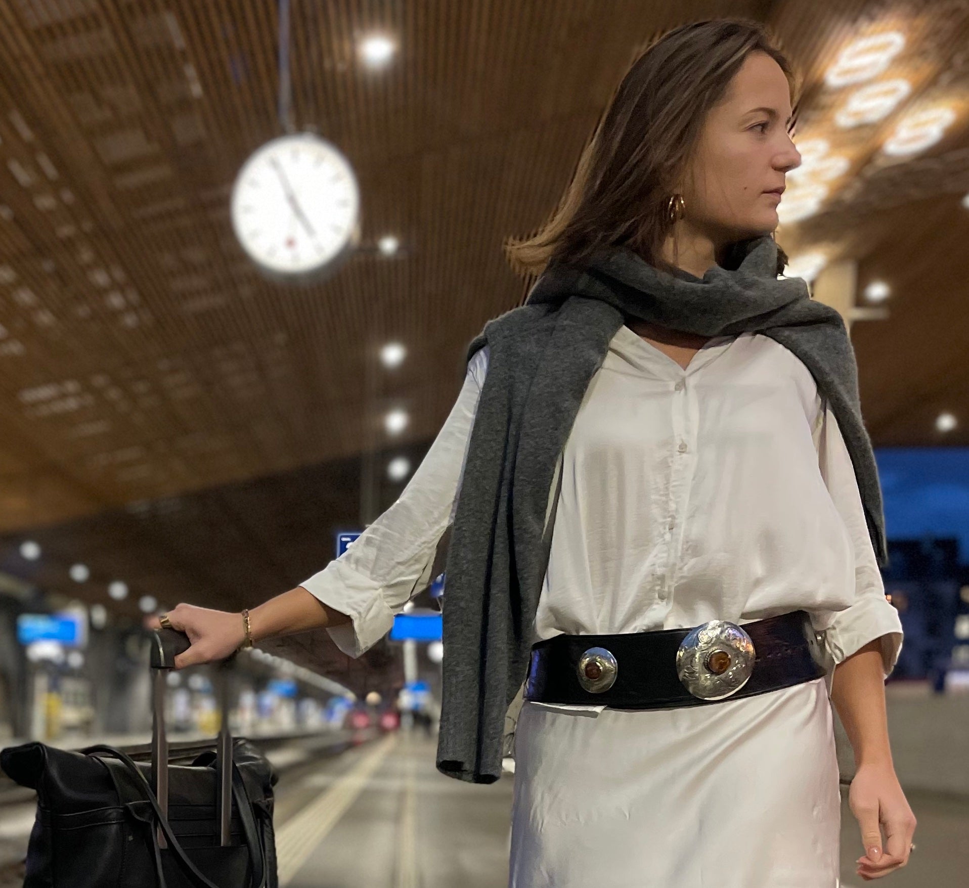 Eine Frau trägt einen schwarzen Ledergürtel mit Metallapplikationen, neben ihr steht die schwarze Shopper-Tasche aus Leder.