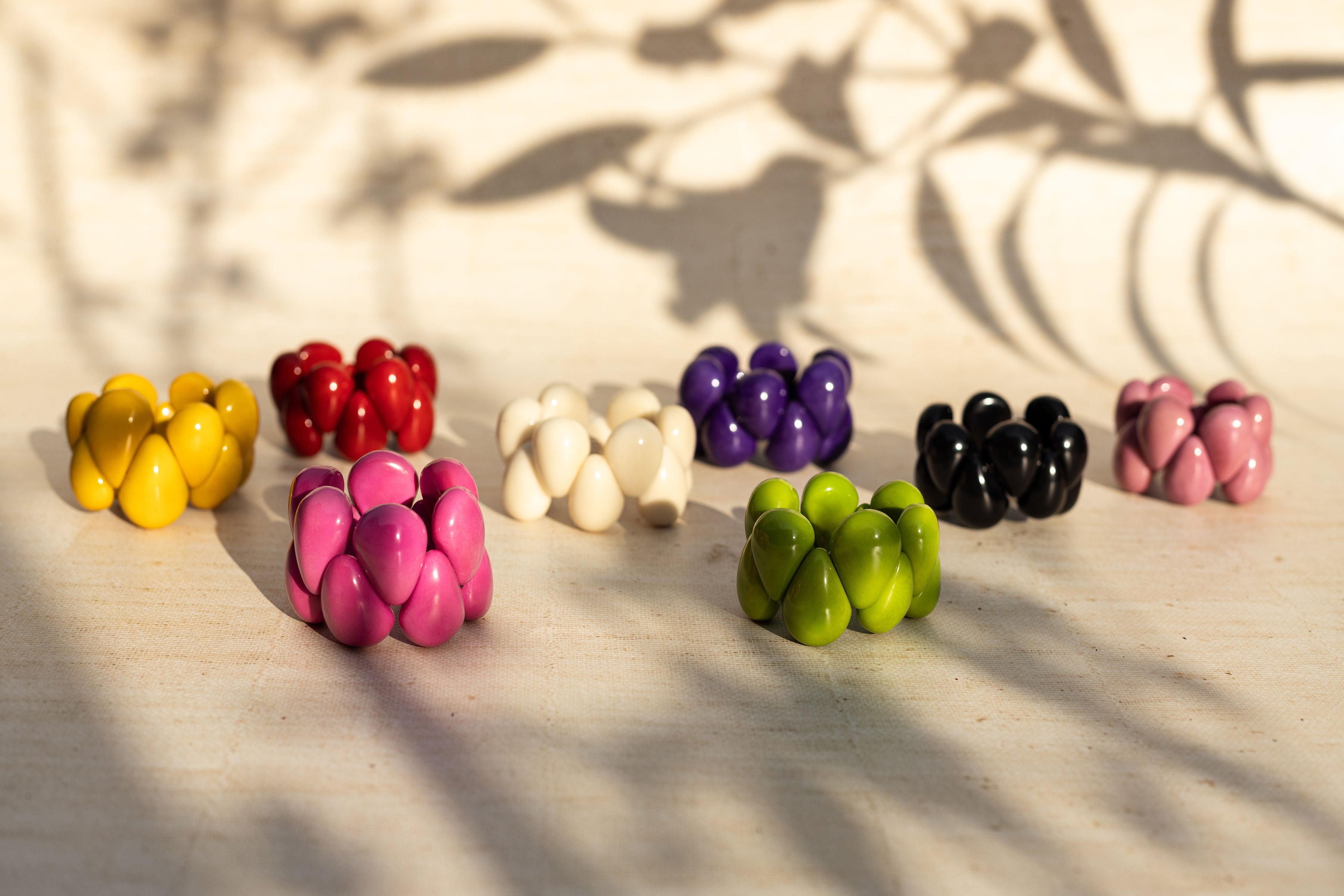 Tagua Armbänder in verschiedenen Farben liegen nebeneinander im Schatten von Pflanzen.