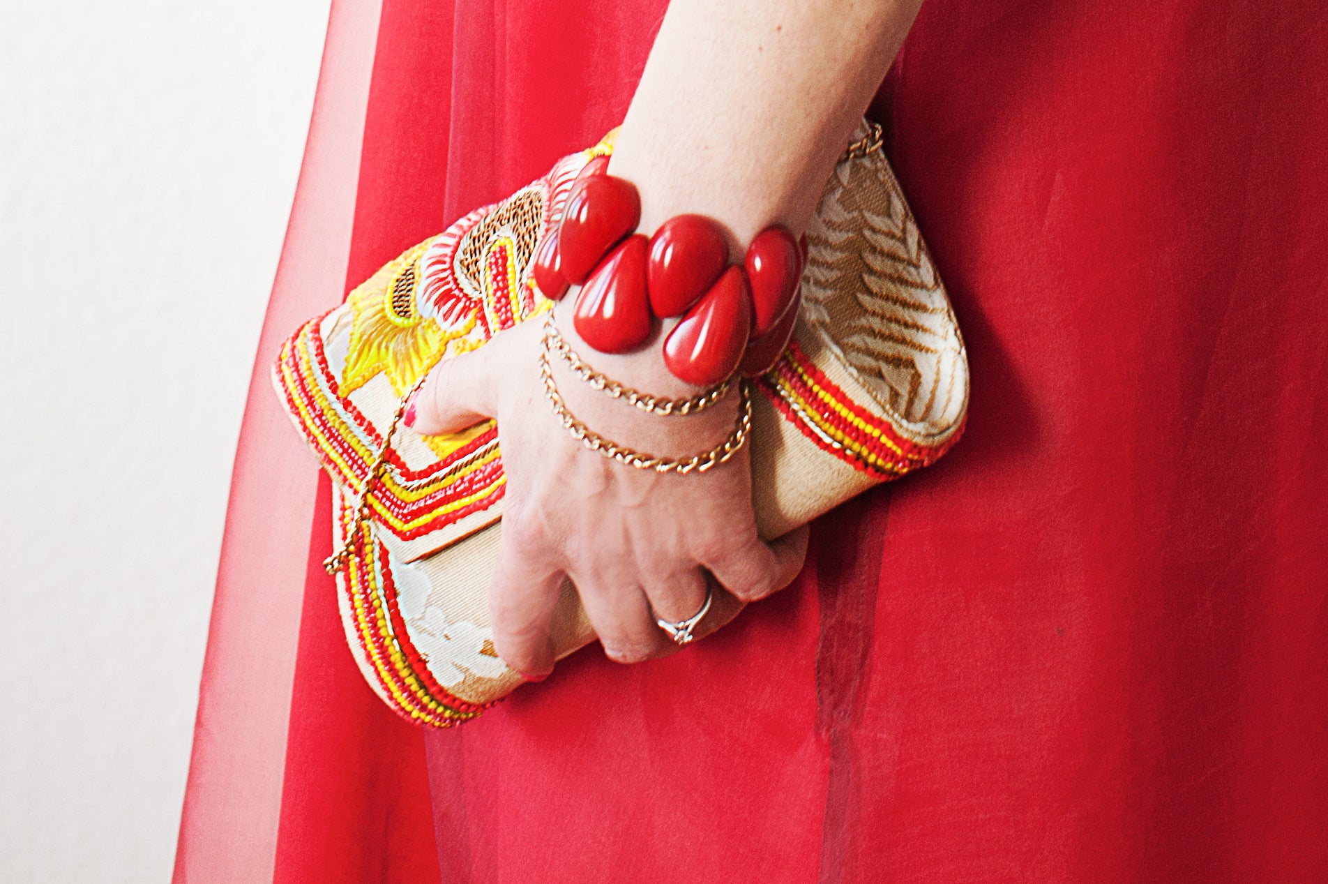 Frauenhand hält eine Clutch und trägt ein rotes Tagua Armband am Handgelenk