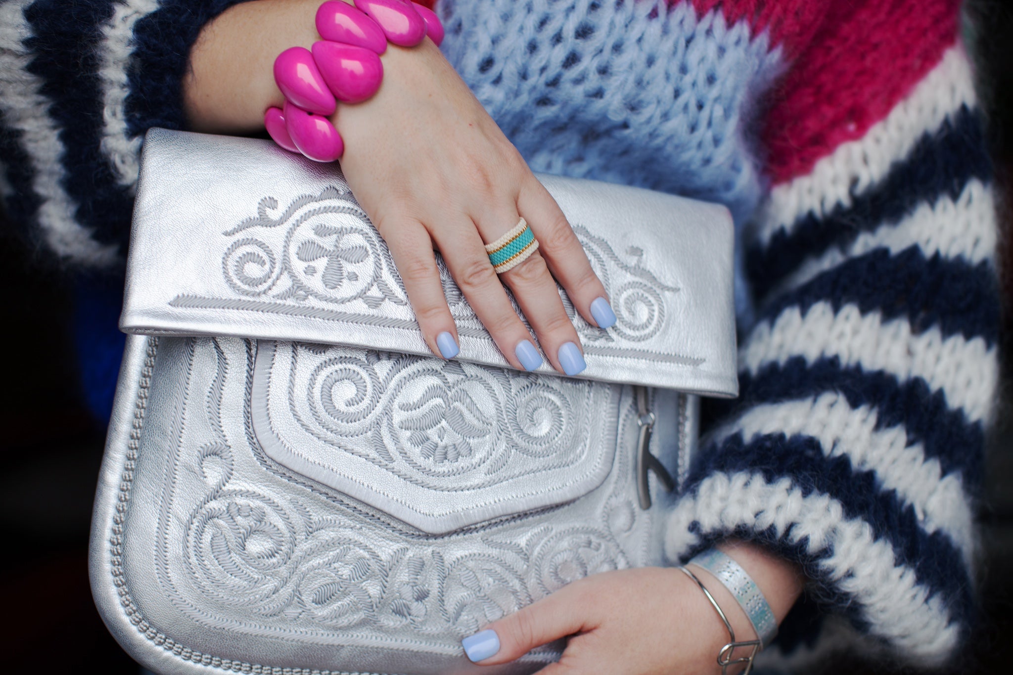 Weibliche Hand hält eine silberne Berber-Umhängetasche und trägt ein pinkes Tagua-Armband. #farbe_silber