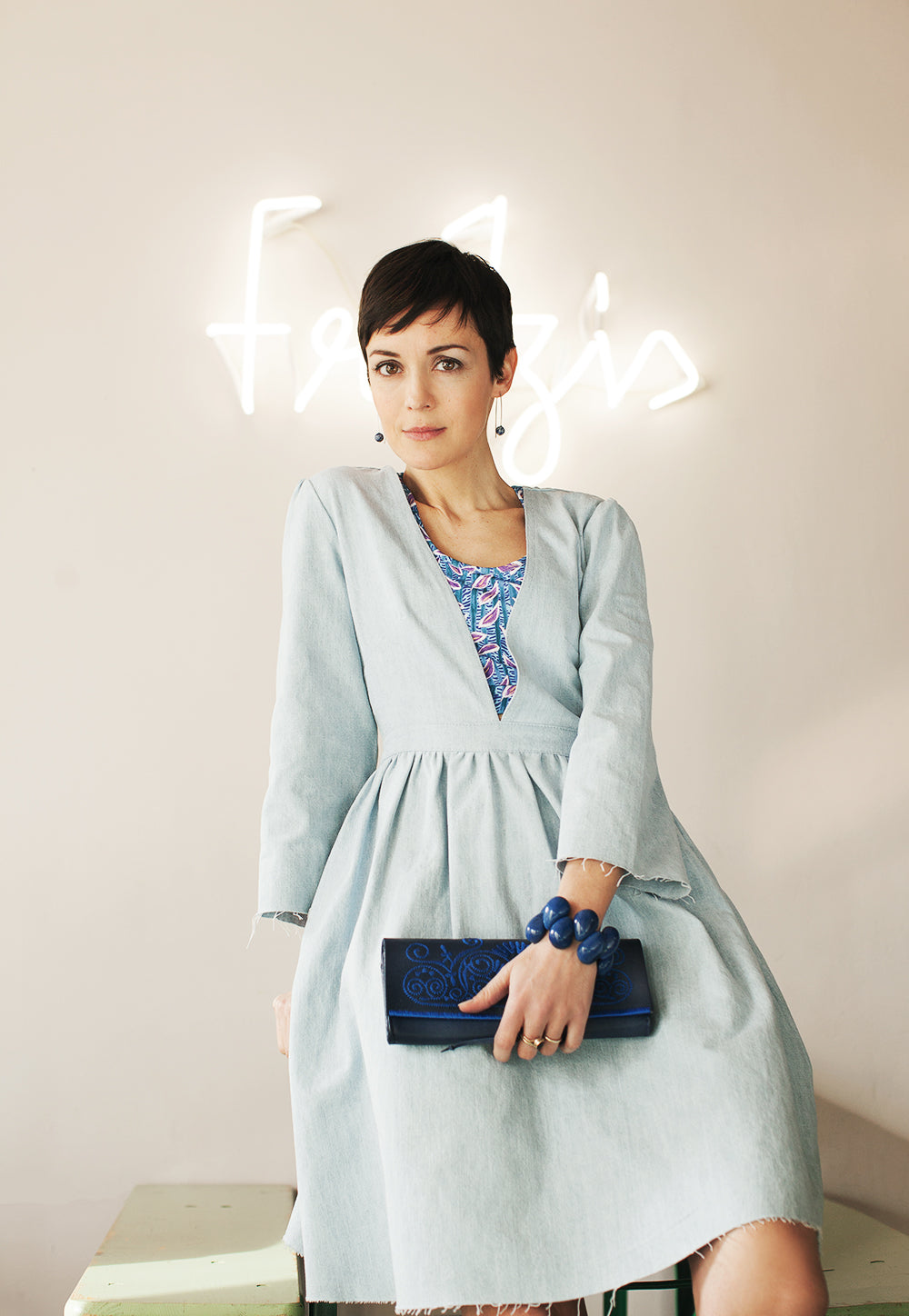 Frau trägt ein blaues Tagua-Armband und eine blaue, bestickte ABURY Clutch.