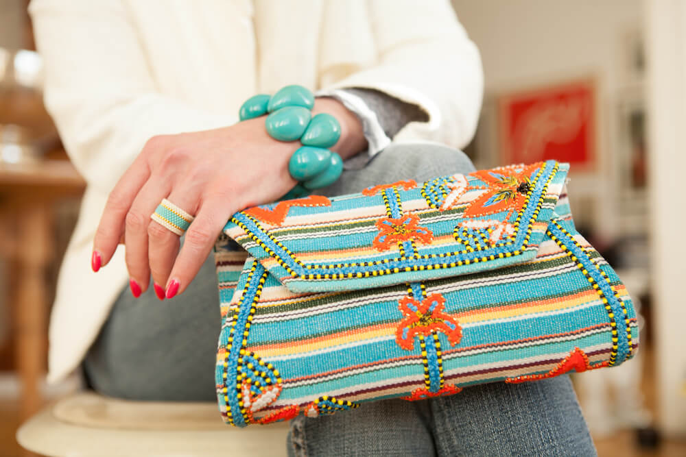 Eine Frau sitzt und hält auf dem Schoß eine blaue Tasche. Sie trägt ein ABURY Tagua-Armband.