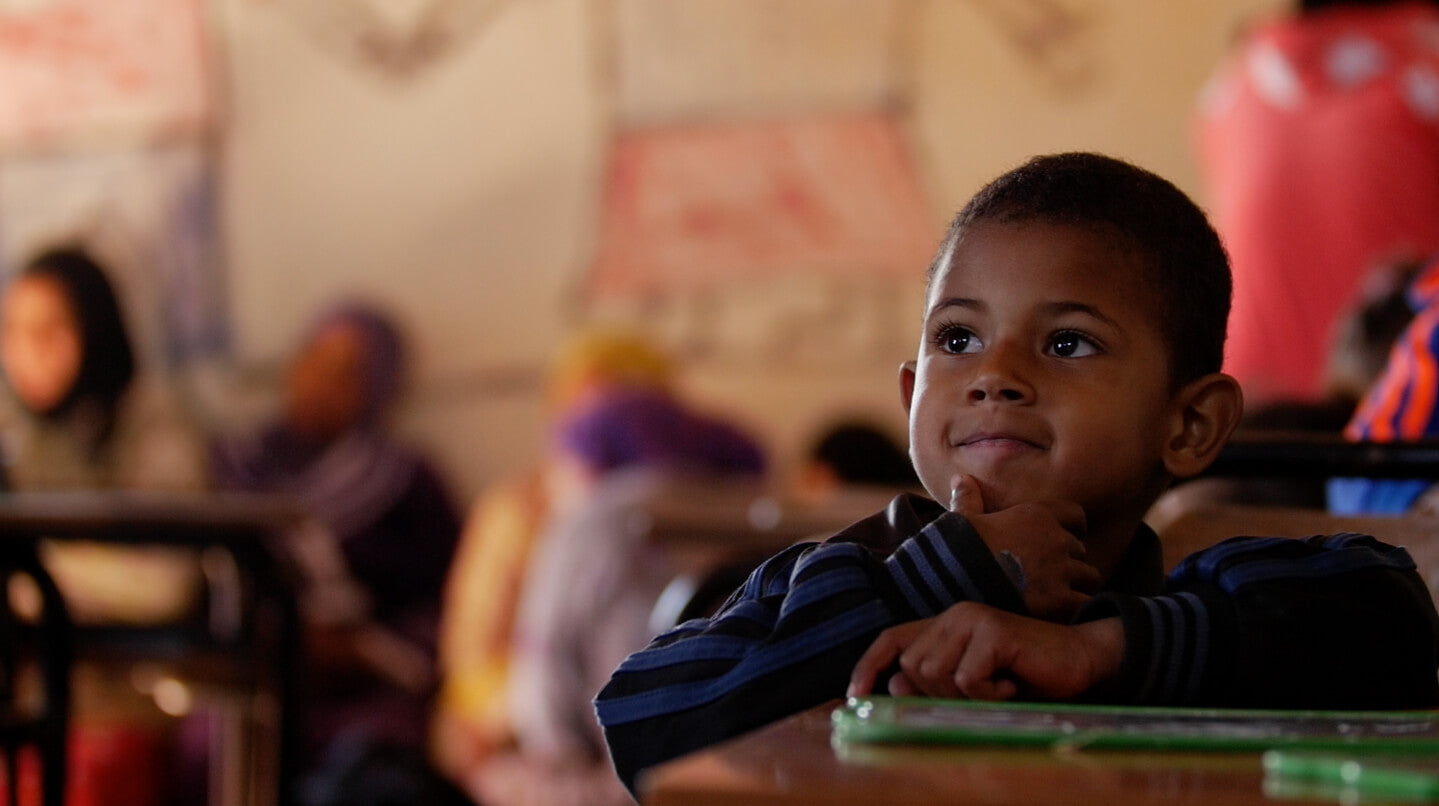 Junge sitzt an der Schulbank und hört aufmerksam zu.