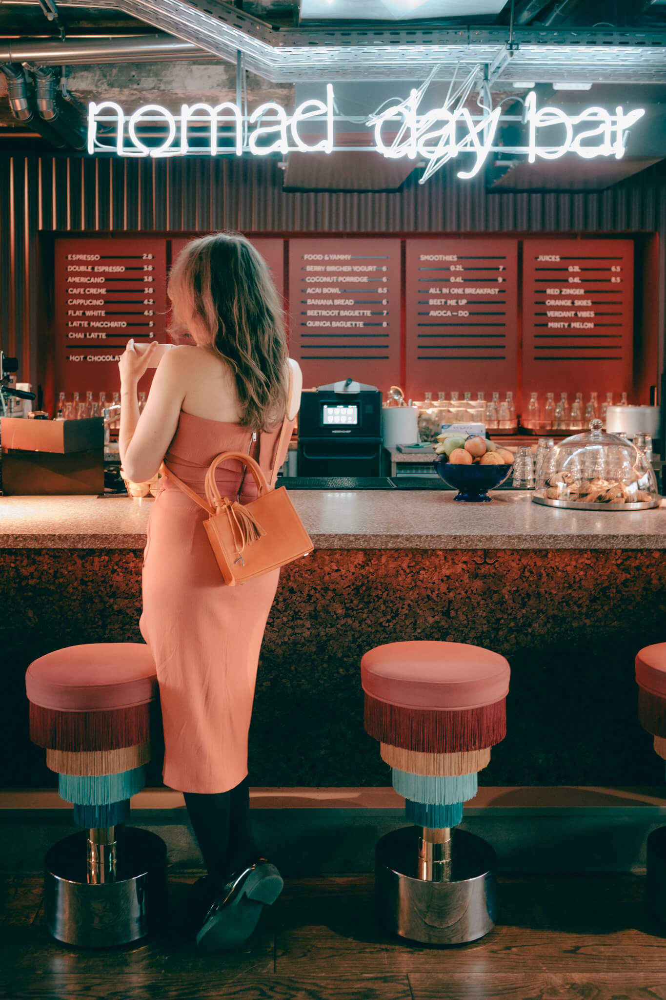 Eine Frau trinkt an der Bar Kaffee und trägt ihre orangefarbene ABURY Mini Tote Bag. #farbe_orange