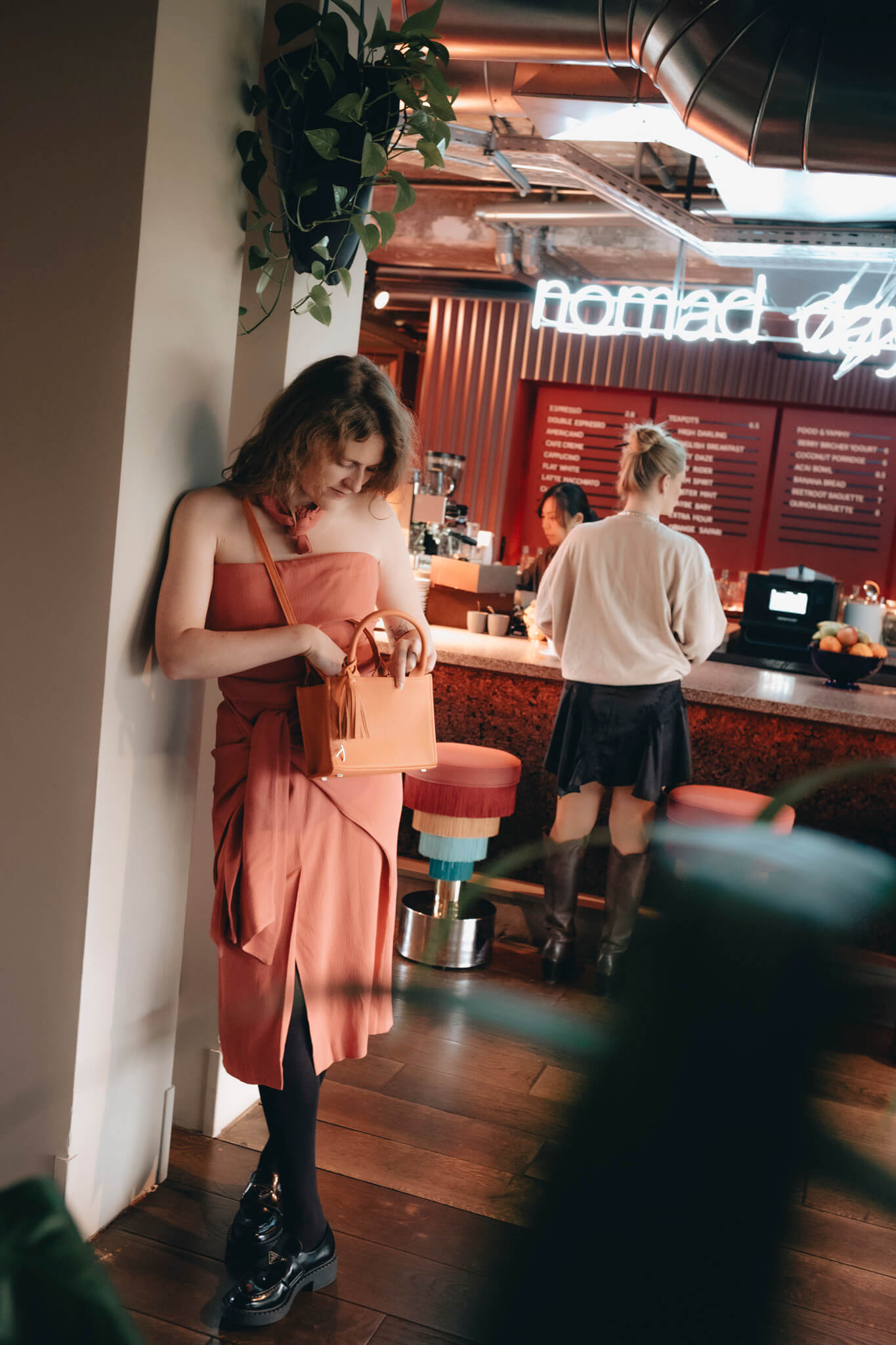 Eine Frau sucht in ihrer orangefarbenen ABURY Mini Tote Bag an der Bar nach etwas. #farbe_orange