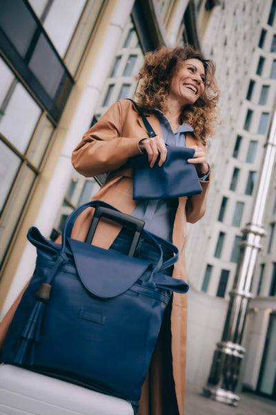 Frau steht neben ihrem weißen Koffer, auf dem der blaue ABURY-Shopper zu sehen ist. #farbe_blau