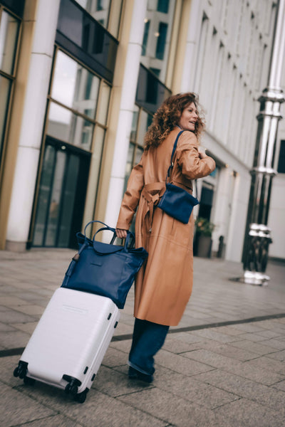 Frau zieht einen weißen Koffer, auf dem der blaue ABURY-Shopper zu sehen ist. #farbe_blau