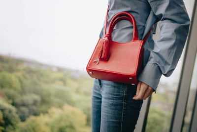 Frau posiert vor einem großen Fenster mit ihrer roten Mini-Tote-Bag. #farbe_rot