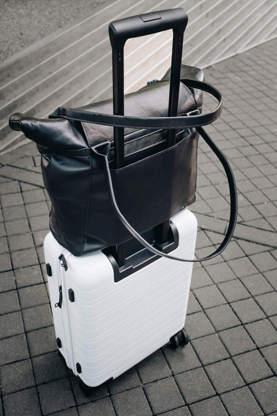 Schwarze ABURY-Shopper auf einem weißen Koffer. #farbe_schwarz