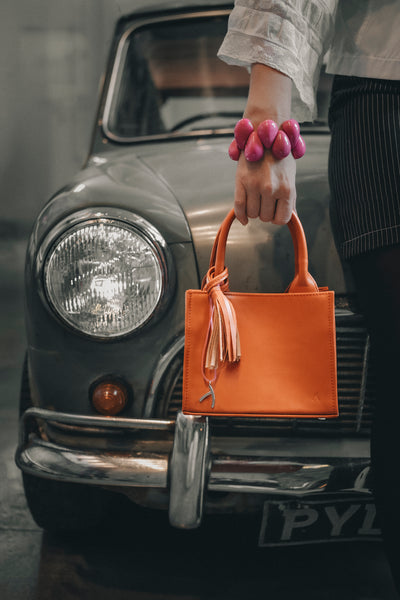Frau posiert mit einer orangefarbenen Mini-Tote-Bag vor einem alten Trabant.