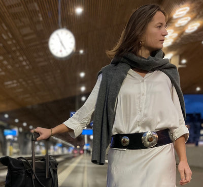 Eine Frau trägt einen schwarzen Ledergürtel mit Metallapplikationen, neben ihr steht die schwarze Shopper-Tasche aus Leder.