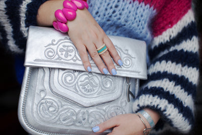 Weibliche Hand hält eine silberne Berber-Umhängetasche und trägt ein pinkes Tagua-Armband. #farbe_silber