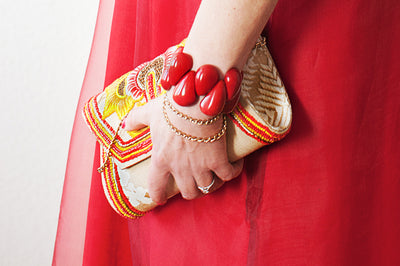 Frauenhand hält eine Clutch und trägt ein rotes Tagua Armband am Handgelenk #farbe_rot