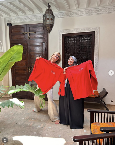 Stolz zeigen zwei Frauen die roten Langarmshirts der ABURY Hospitality Academy in die Kamera.
