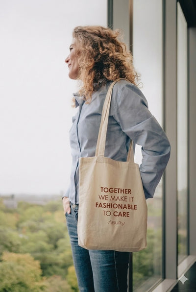Die Frau trägt den ABURY-Jutebeutel mit der Aufschrift „Together we make it fashionable to care”.