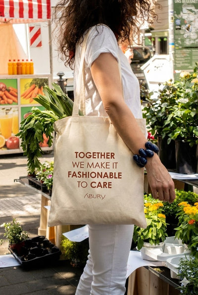 Die Frau trägt den ABURY-Jutebeutel mit der Aufschrift „Together we make it fashionable to care”.