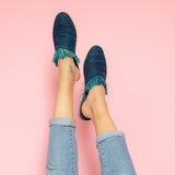 feet model in front of a pink background wearing jeans and abury blue raffia summer slippers with fringes